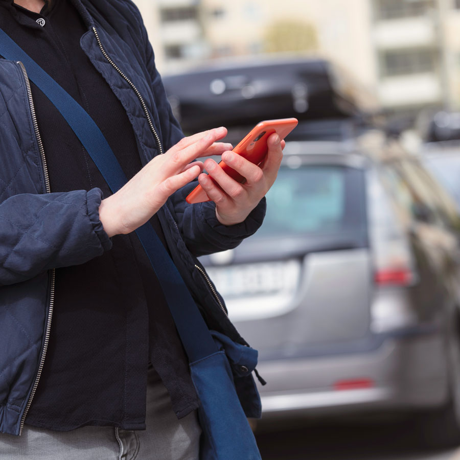Bild på person som använder en mobiltelefon bakom en bil